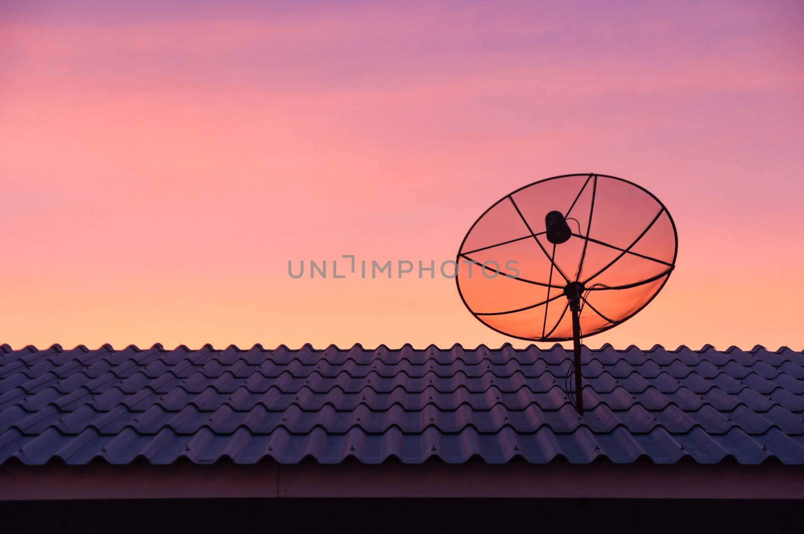 Silhouetted satellite dish on the roof in sunset sky