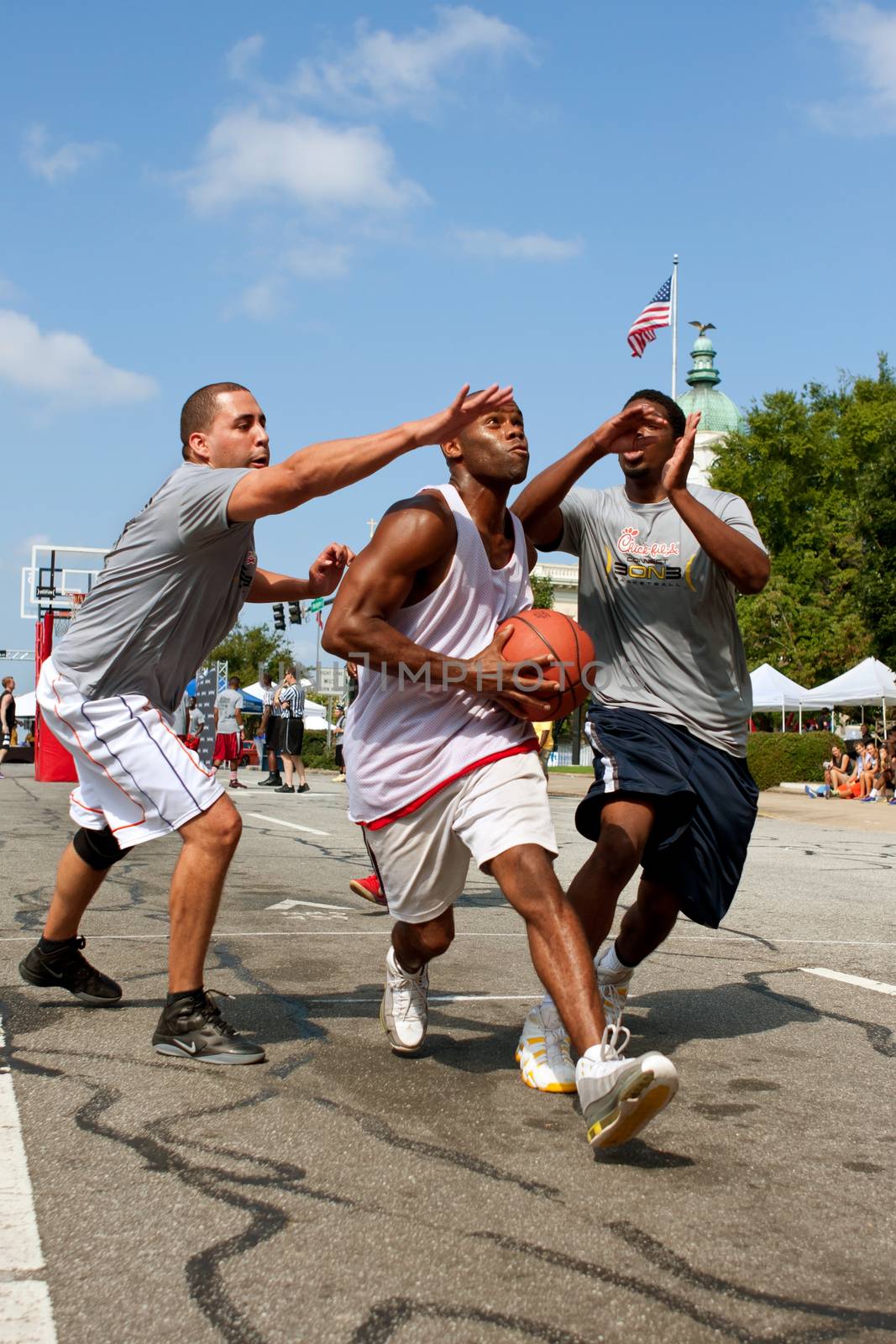 Athens, GA, USA - August 24, 2013:  A young man splits two defenders while driving to the hoop in a 3-on-3 basketball tournament held on the streets of downtown Athens.