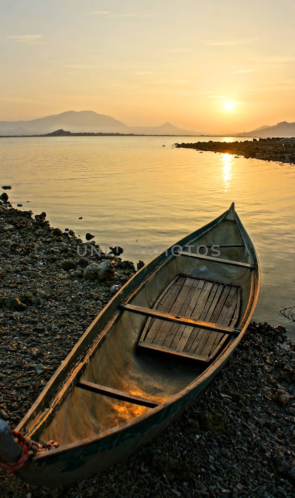 Lonely boat looking toward the sun, sunrise at horizon with yellow sky, boat on stone shore, calm, beautiful  sightseeing in morning at sea