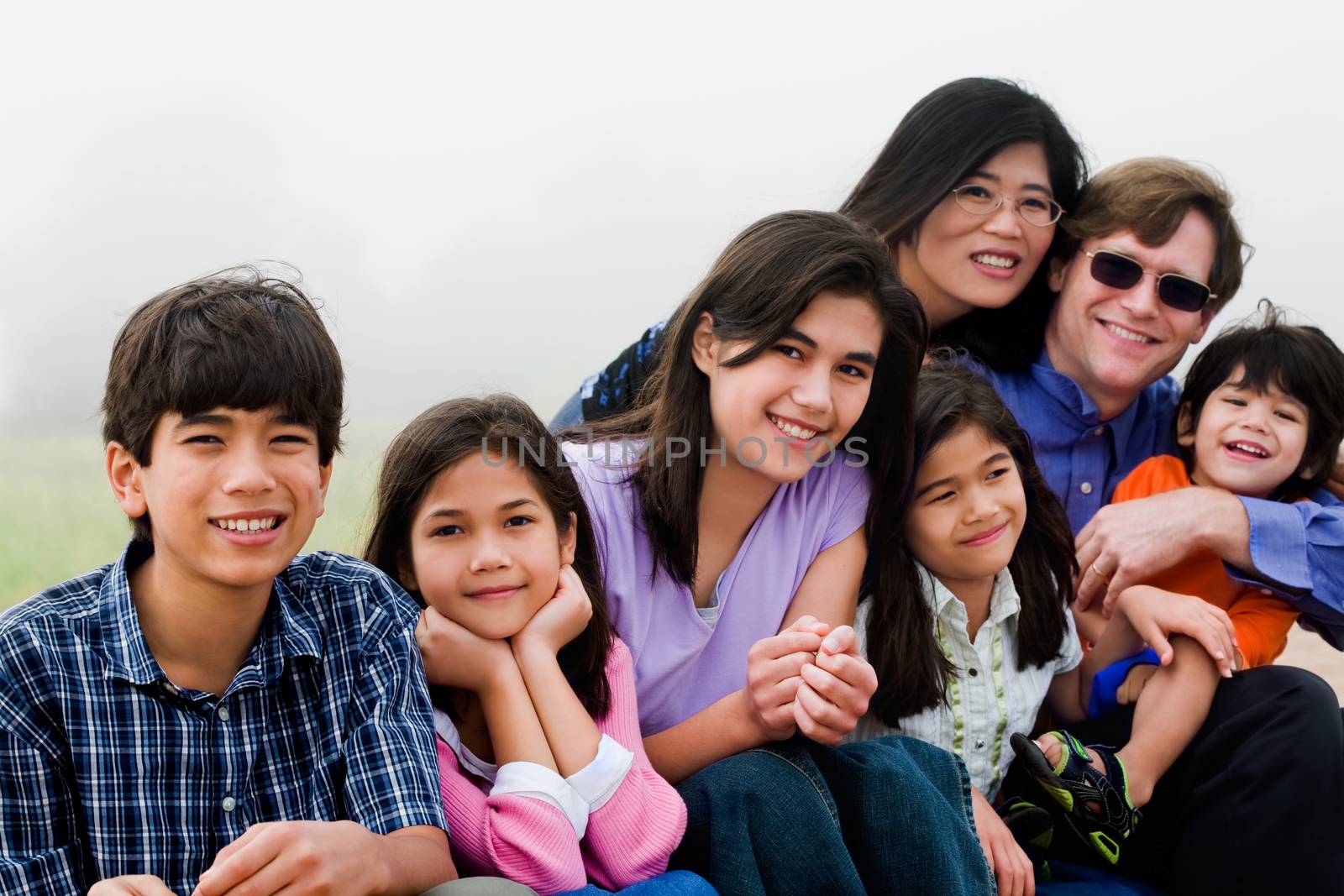 Multiracial family of seven sitting on foggy beach