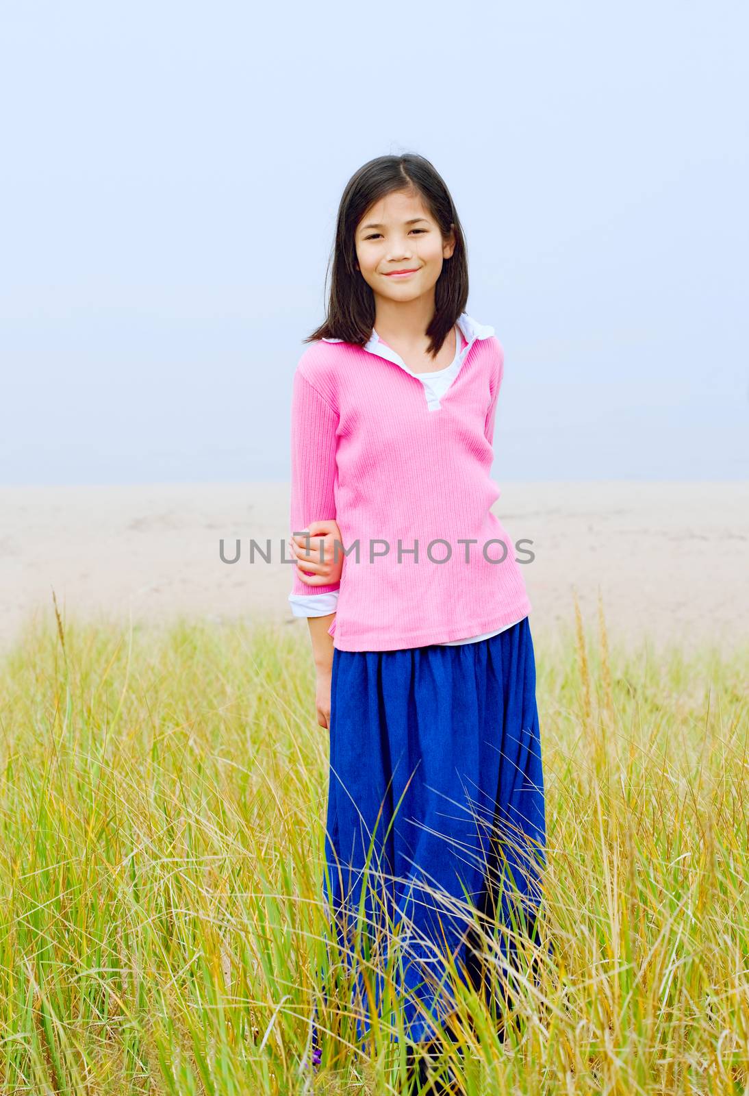 Girl standing in tall grassy field on  a misty day by beach