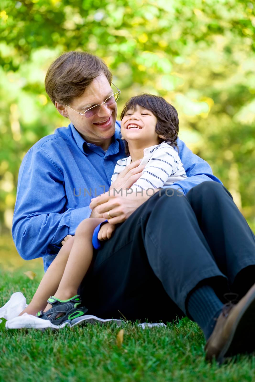 Businessman holding his disabled son on grass. Child has cerebral palsy.