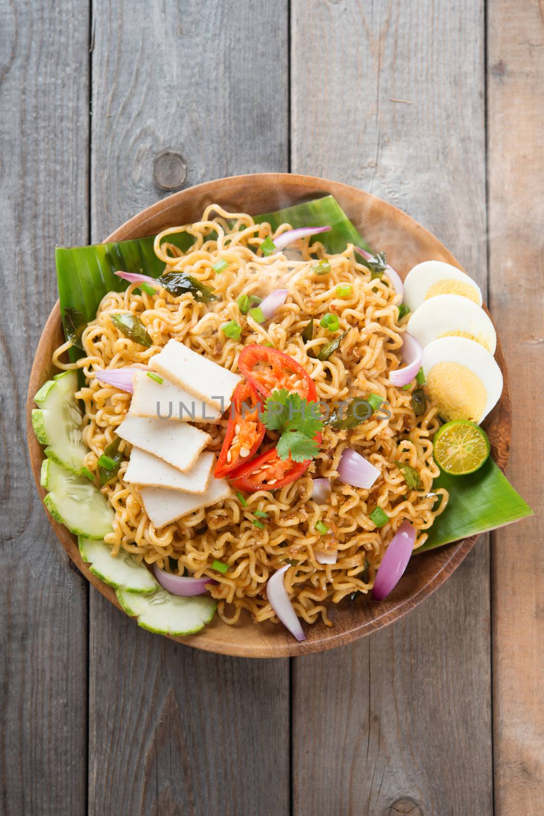 Malaysian style maggi goreng mamak  or spicy dried curry instant noodles.  Asian cuisine, ready to serve on wooden dining table setting. Fresh hot with steamed smoke.