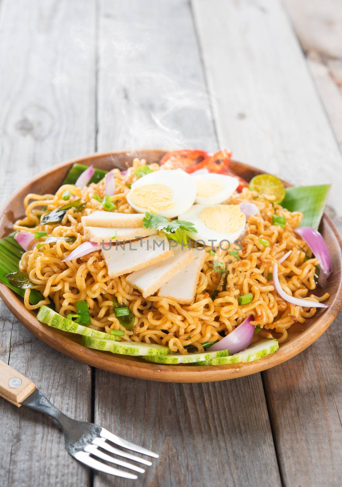 Spicy dried curry instant noodles or Malaysian style maggi goreng mamak.  Asian cuisine, ready to serve on wooden dining table setting. Fresh hot with steamed smoke.