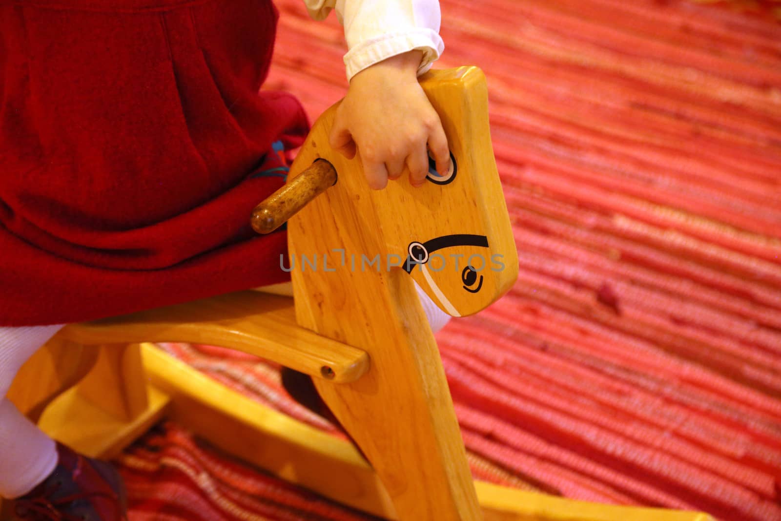 A small girl dressed in red is riding a wooden horse.