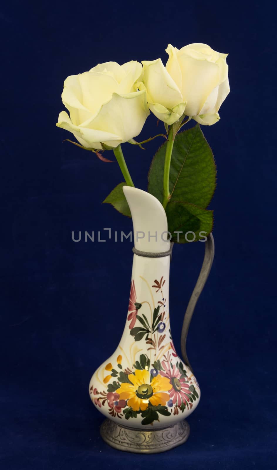 two white roses in a decorated vase with blue background