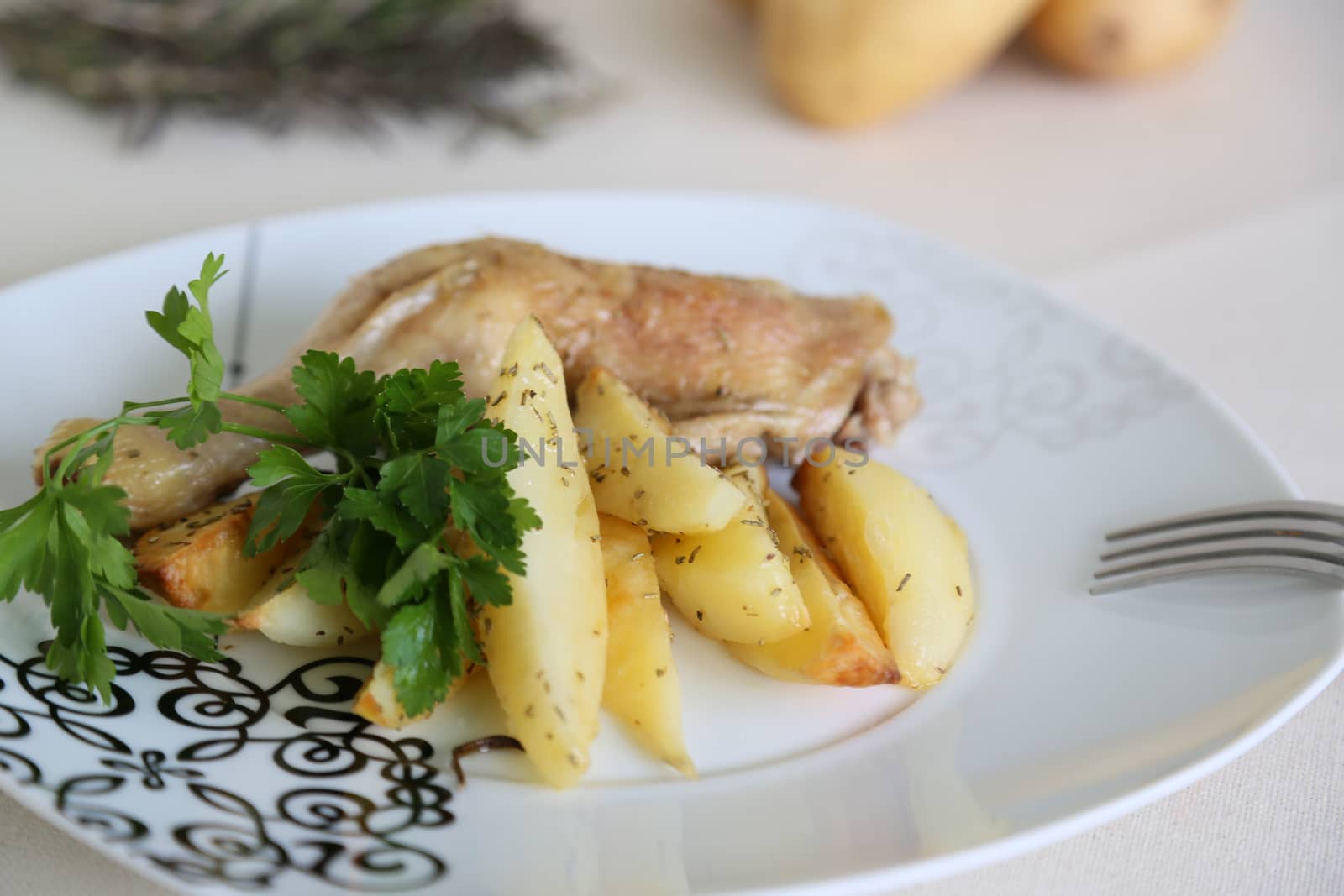 A plate with baked potatoes, chicken, fresh parsley with a fork on the plate