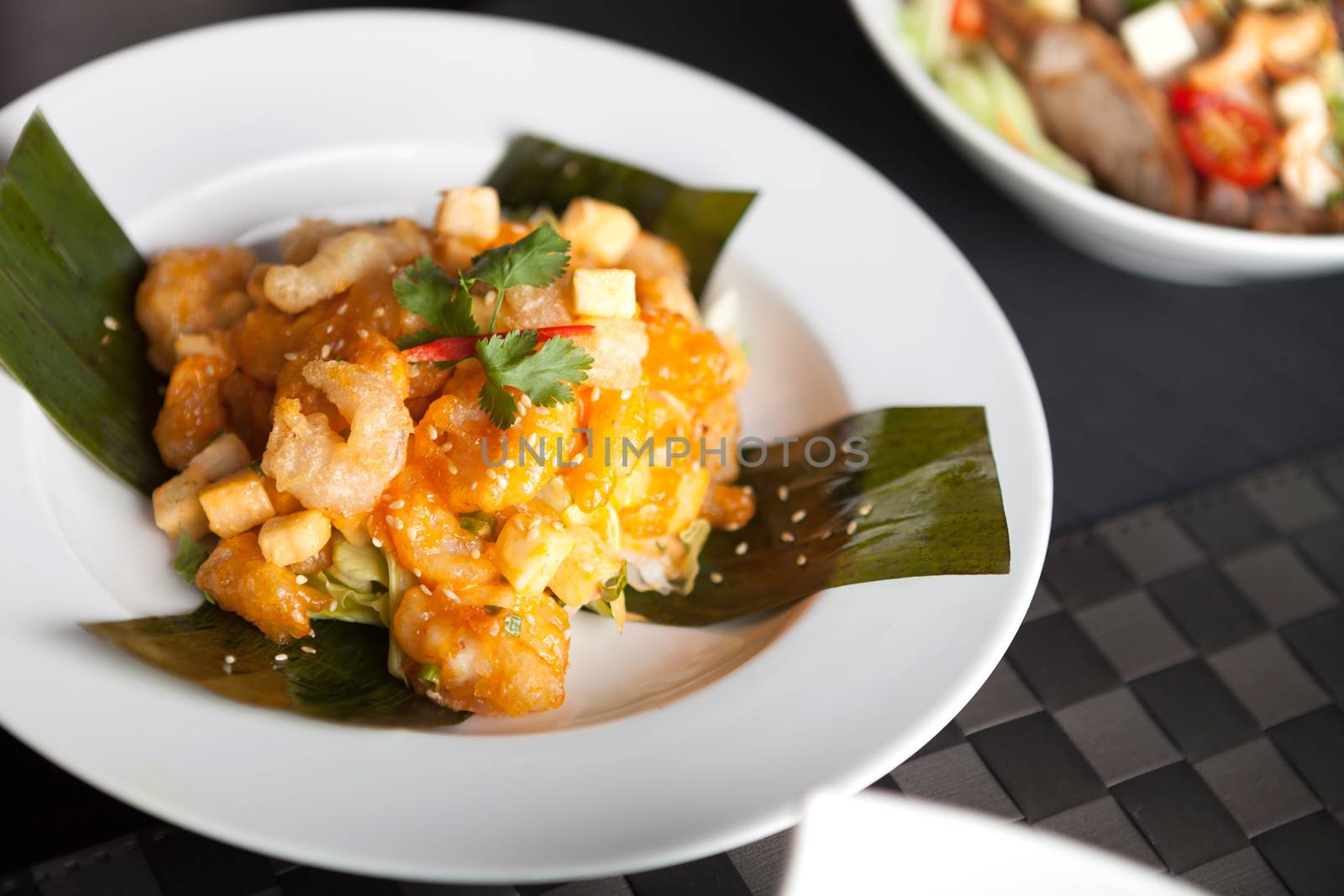 Thai crispy shrimp dish with apple and sesame seeds presented beautifully on a white square plate with chopsticks.