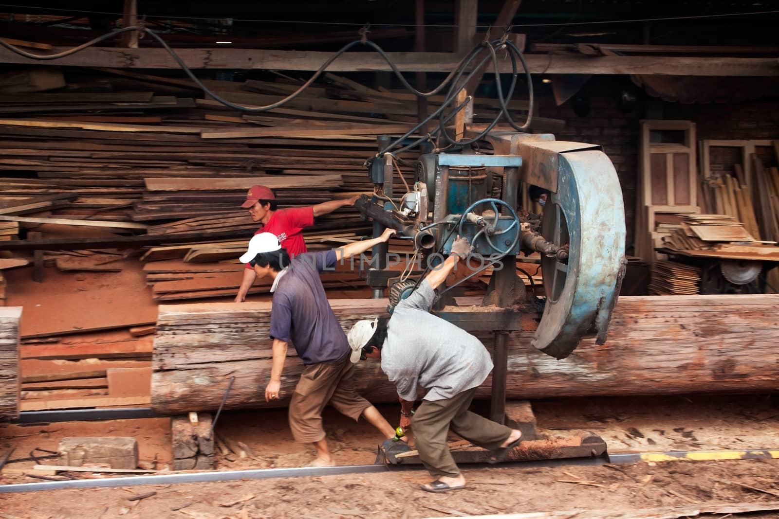 Quy Nhon, Viet Nam: Three woodworker try to pull cumbersome machine to split section of a tree trunk into plank at sawmill. Vietnam, June 18, 2012