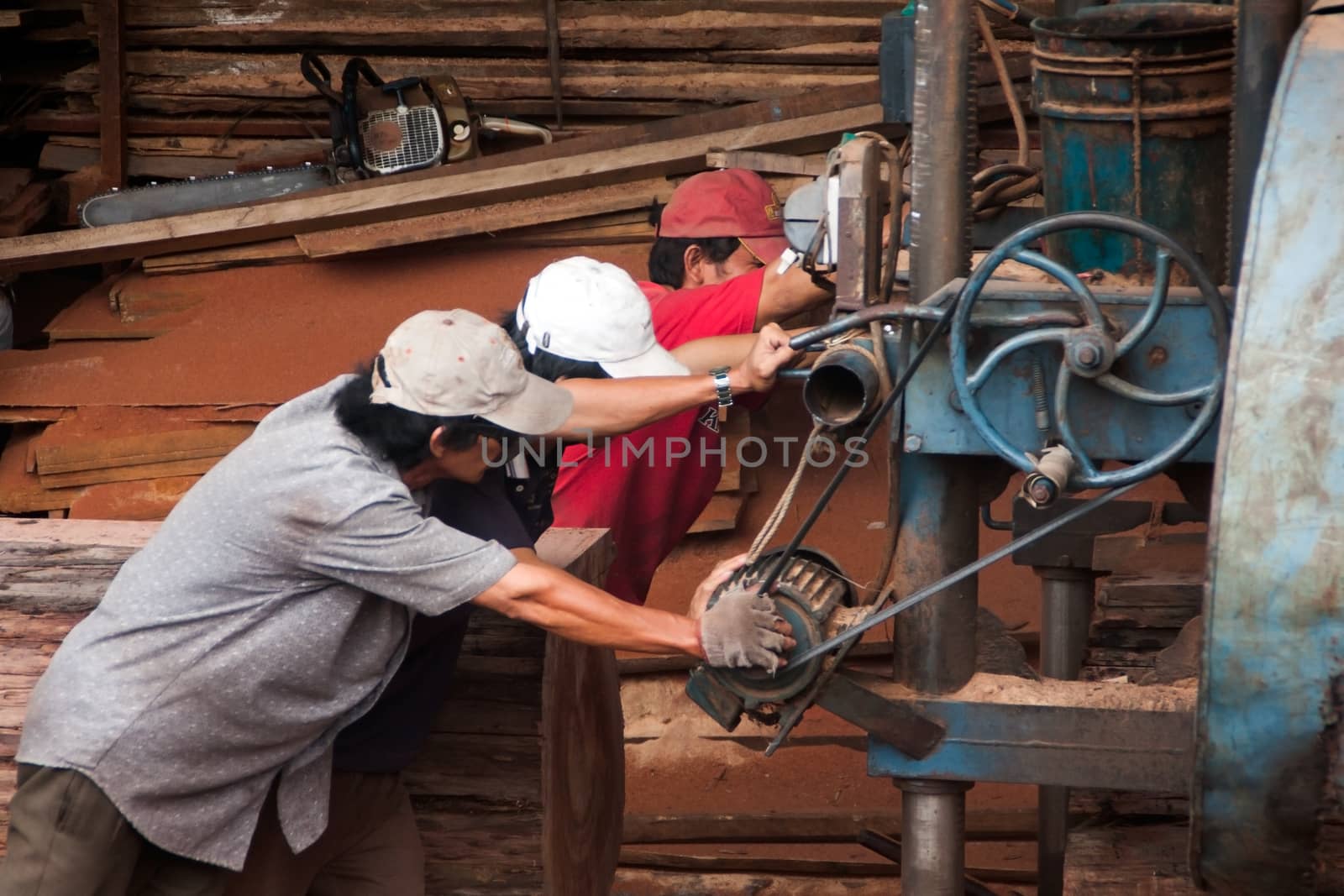 Quy, Nhon, viet Nam: Three woodworker try to push cumbersome machine to split section of a tree trunk into plank at sawmill. Vietnam, June 18, 2012