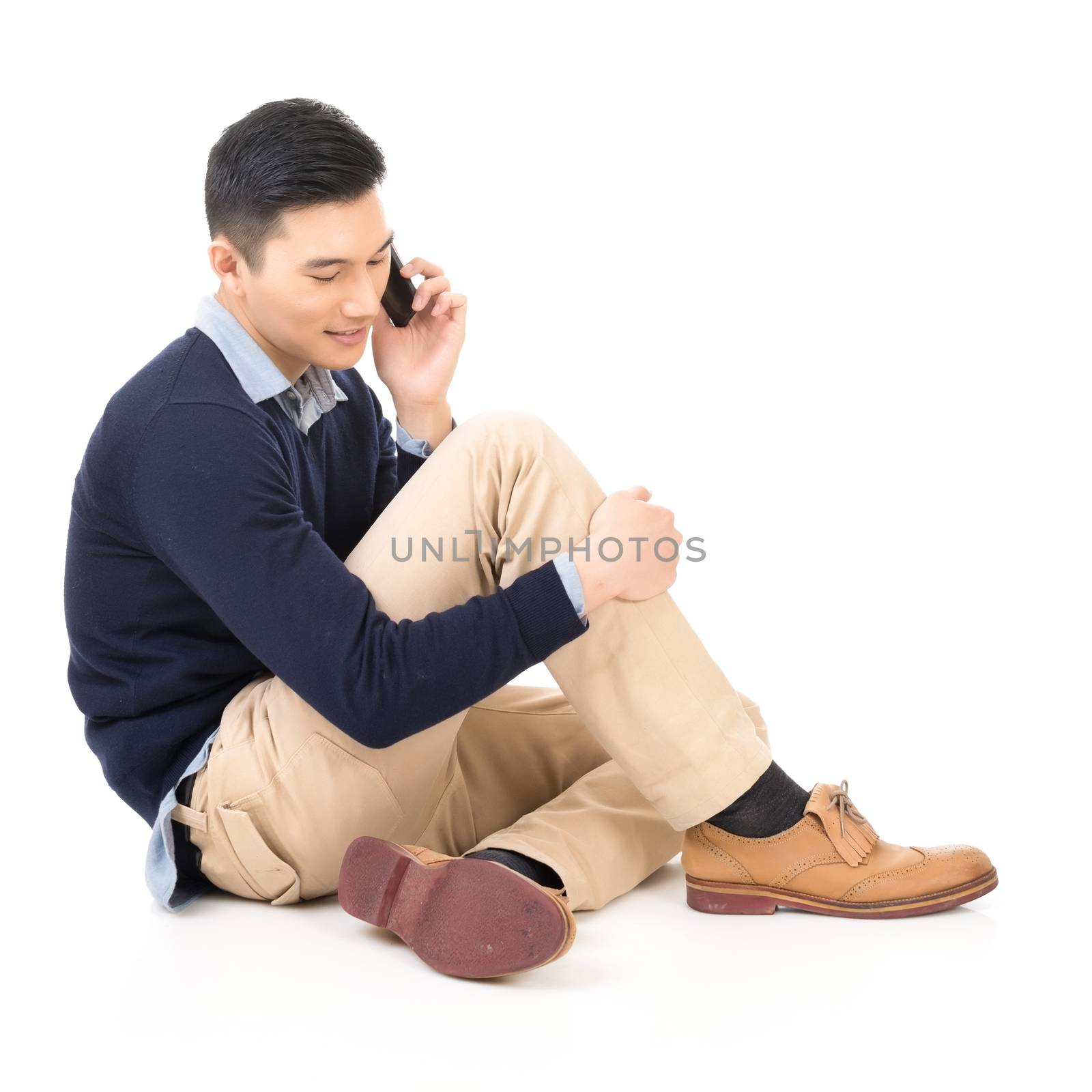 Handsome Asian guy sit and take a call, full length portrait isolated on white background.