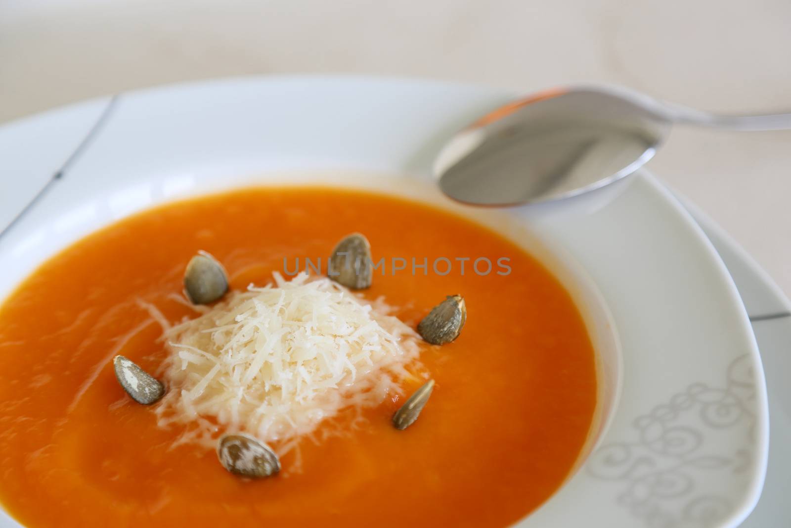 a plate of pumpkin cream soup with pumpkin seed and parmesan cheese.