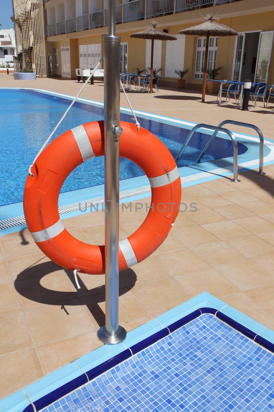 Orange lifebuoy or lifebelt hanging next to the swimming pool of a hotel.