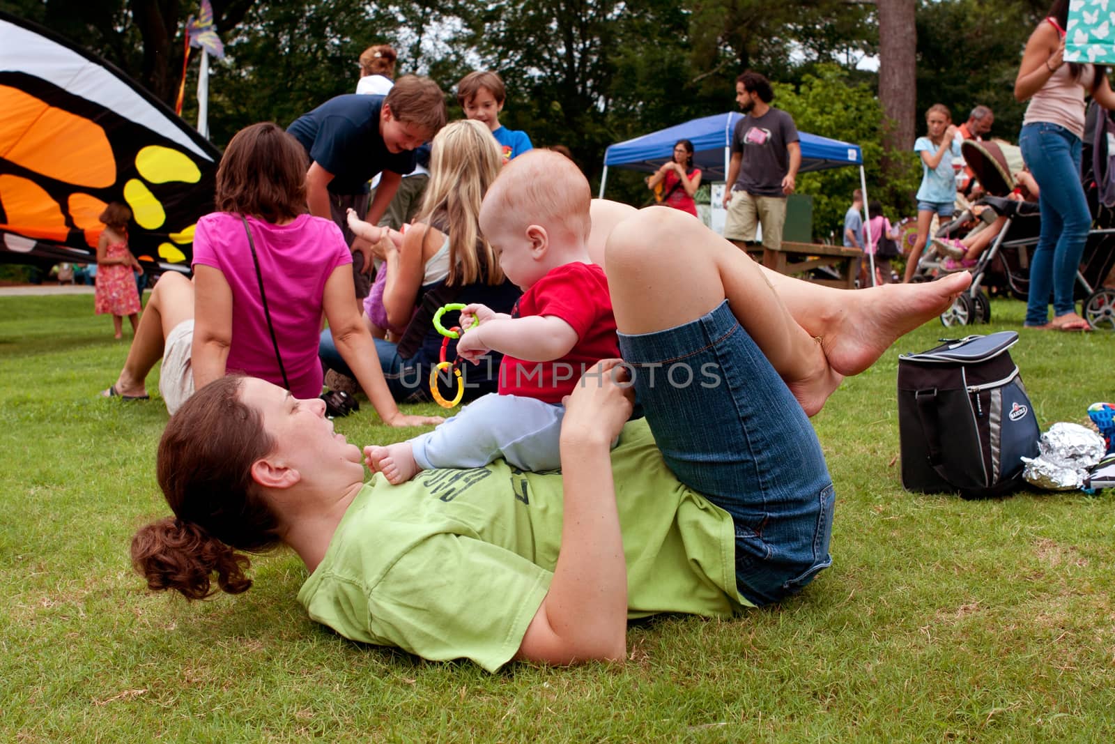 Mother Plays With Baby While Laying On Grass At Festival by BluIz60