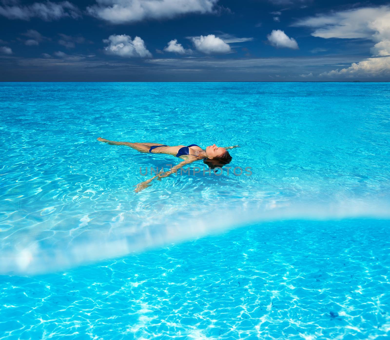 Woman in bikini lying on water at tropical beach