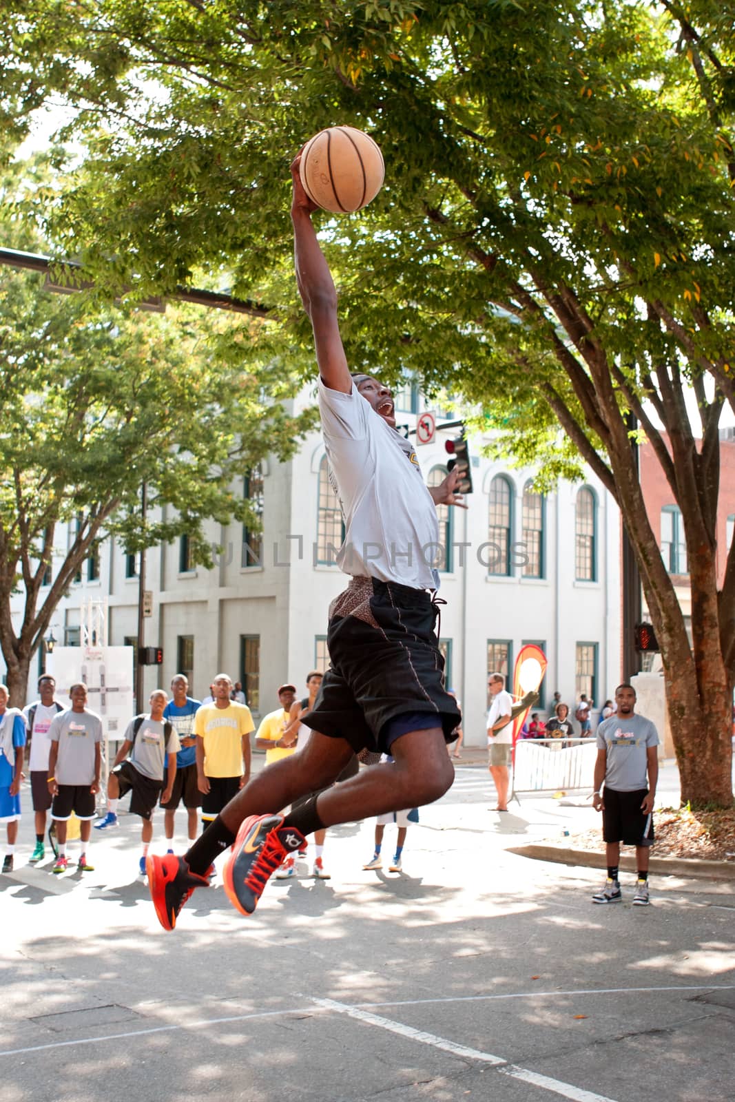 Young Man Leaps To Dunk Basketball During Outdoor Street Tournament by BluIz60