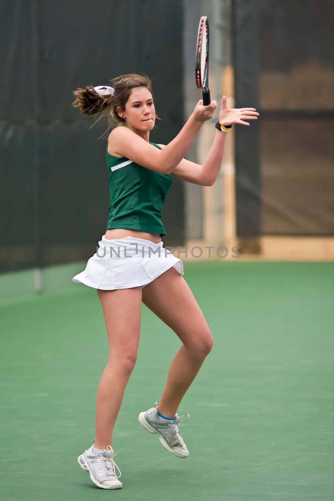 A female high school tennis player follows through after hitting a forehand in match.