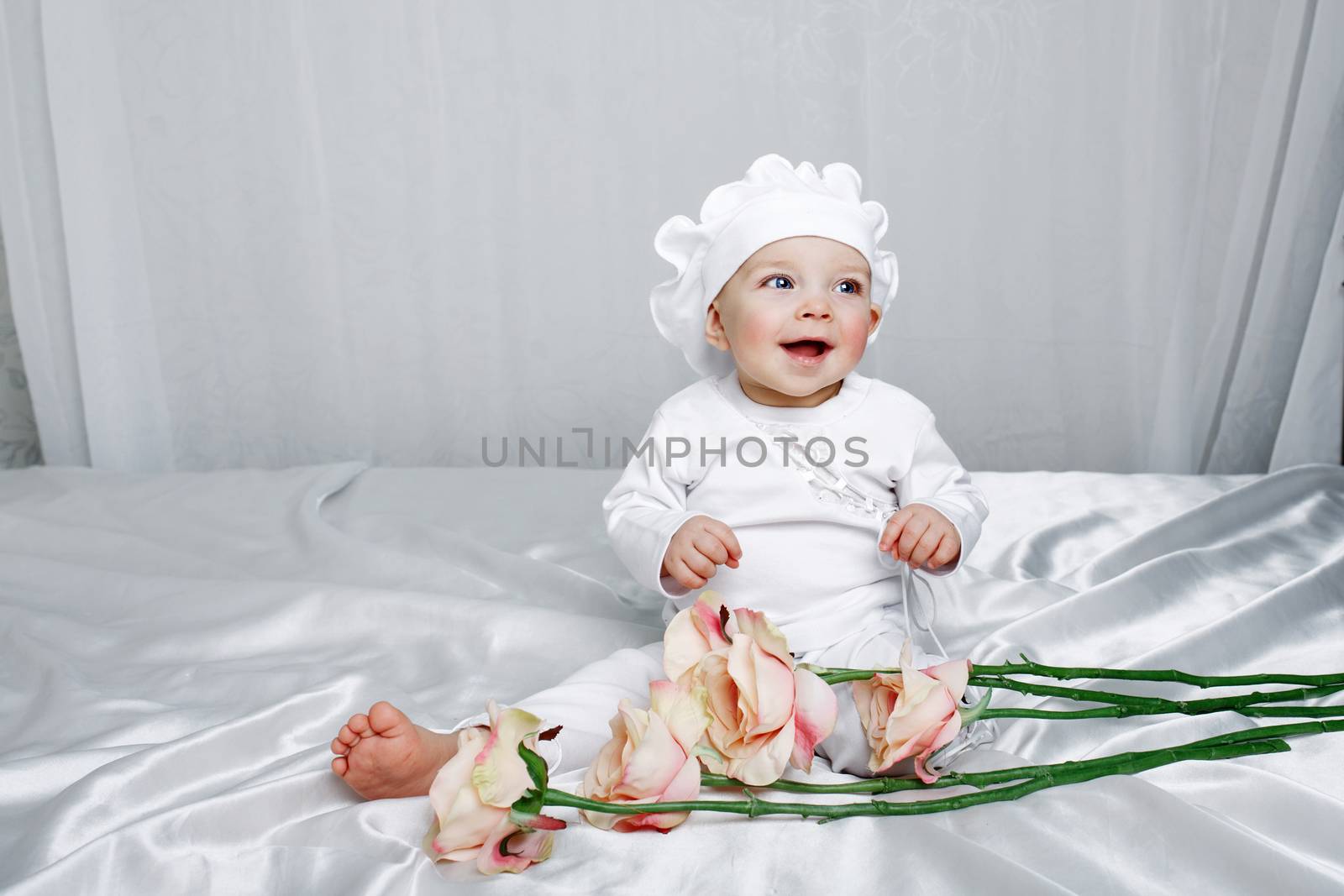 Little girl sitting on silk sheets lie at the feet of flowers