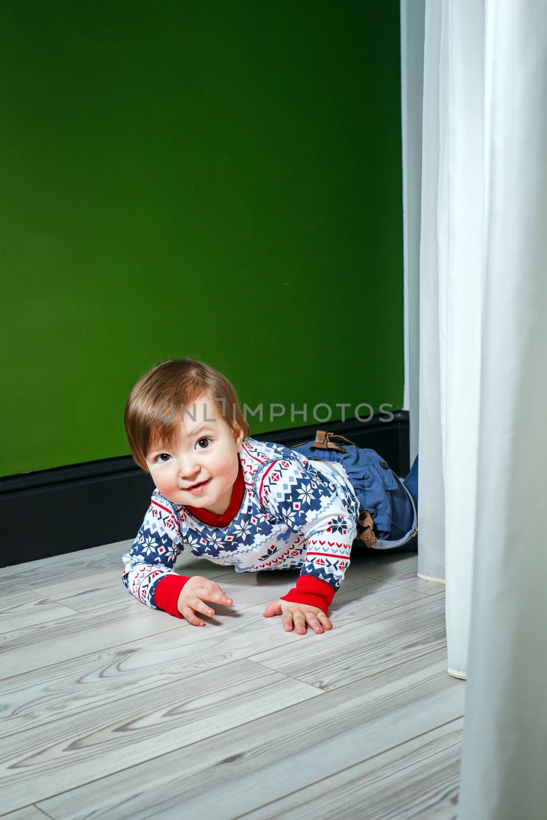 Little boy in a sweater and jeans at home on a wooden floor