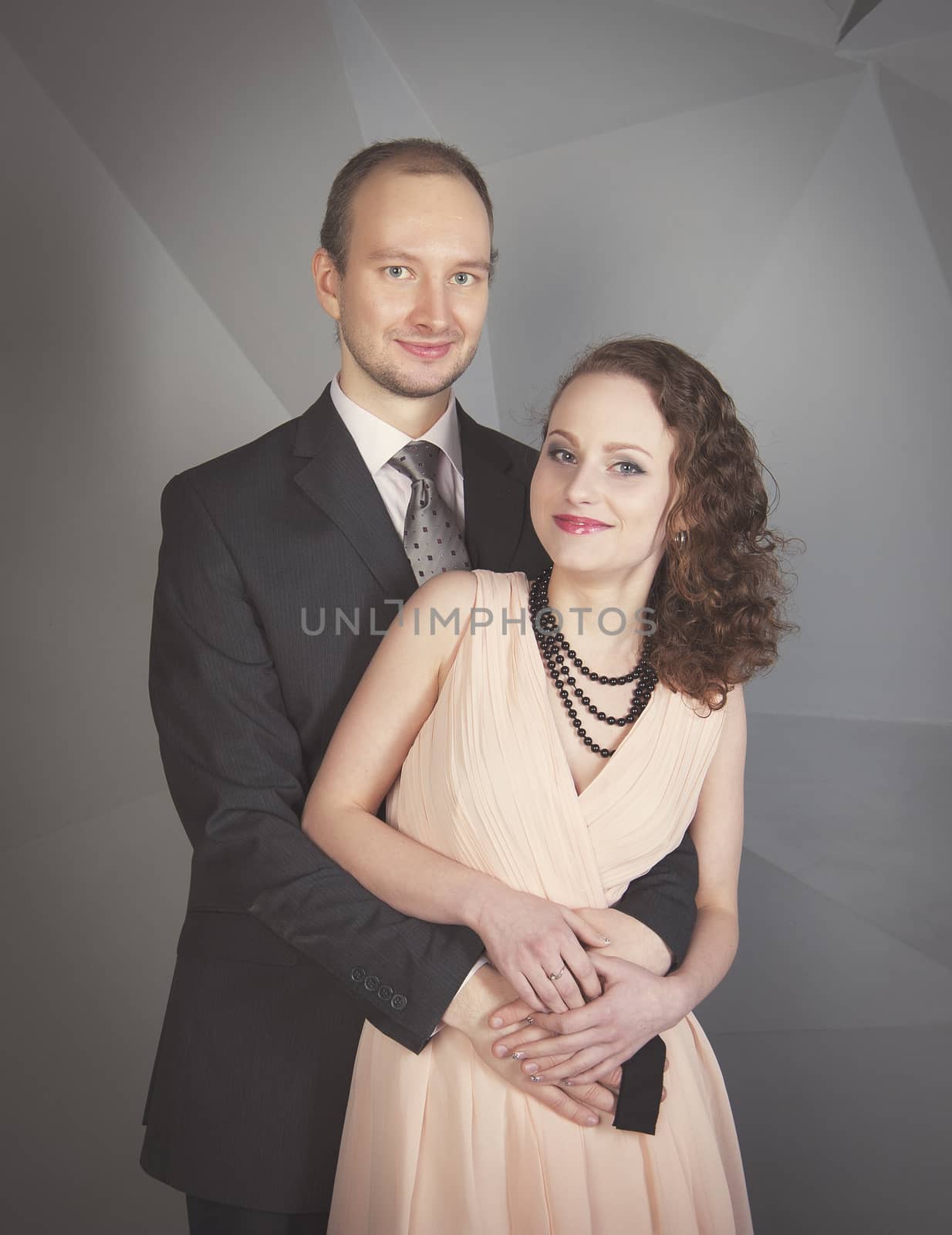 young man gently embraces a girl on a grey background