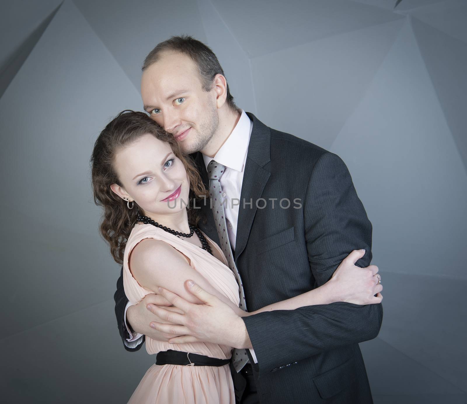 young man gently embraces a girl on a grey background