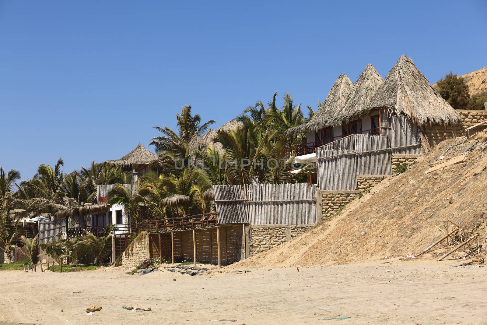 MANCORA, PERU - AUGUST 17, 2013: Thatched roof accomodation with palm trees along the sandy beach on August 17, 2013 in Mancora, Peru. Mancora is one of the most popular beach towns of Peru. 