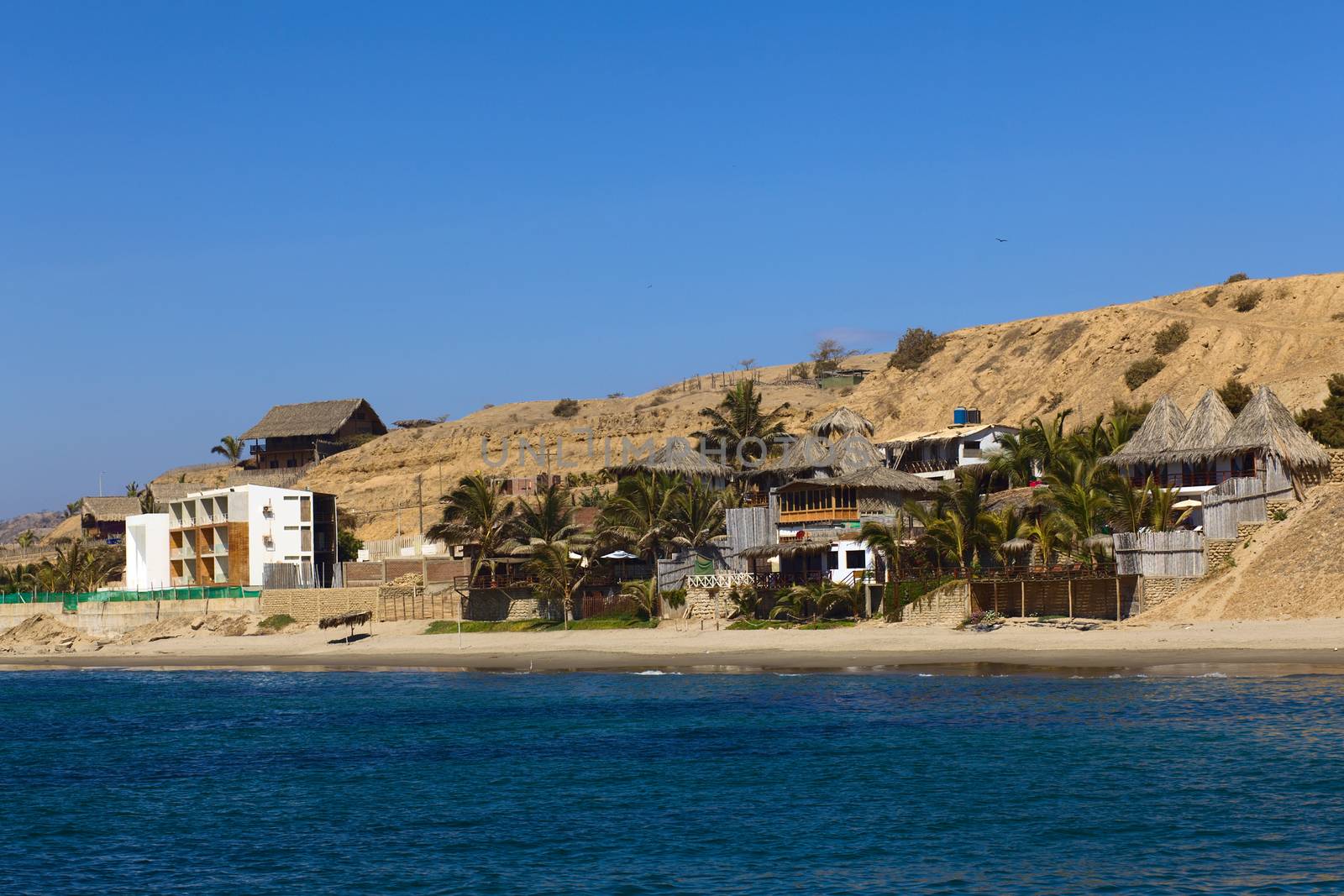 MANCORA, PERU - AUGUST 17, 2013: Thatched roof accomodation with palm trees and a modern building along the sandy beach on August 17, 2013 in Mancora, Peru. Mancora is one of the most popular beach towns of Peru. 