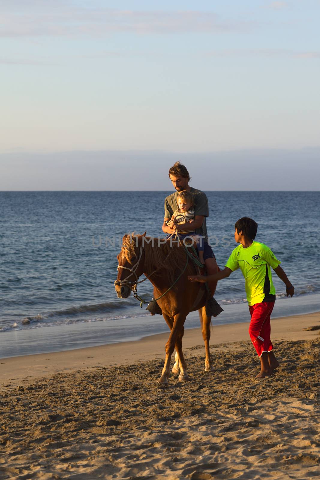 MANCORA, PERU - AUGUST 20, 2013: Unidentified young man and child on horseback, with unidentified boy walking along the horse on the beach on August 20, 2013 in Mancora, Peru. Mancora is a popular beach town in Peru for both Peruvian and foreign tourists.   