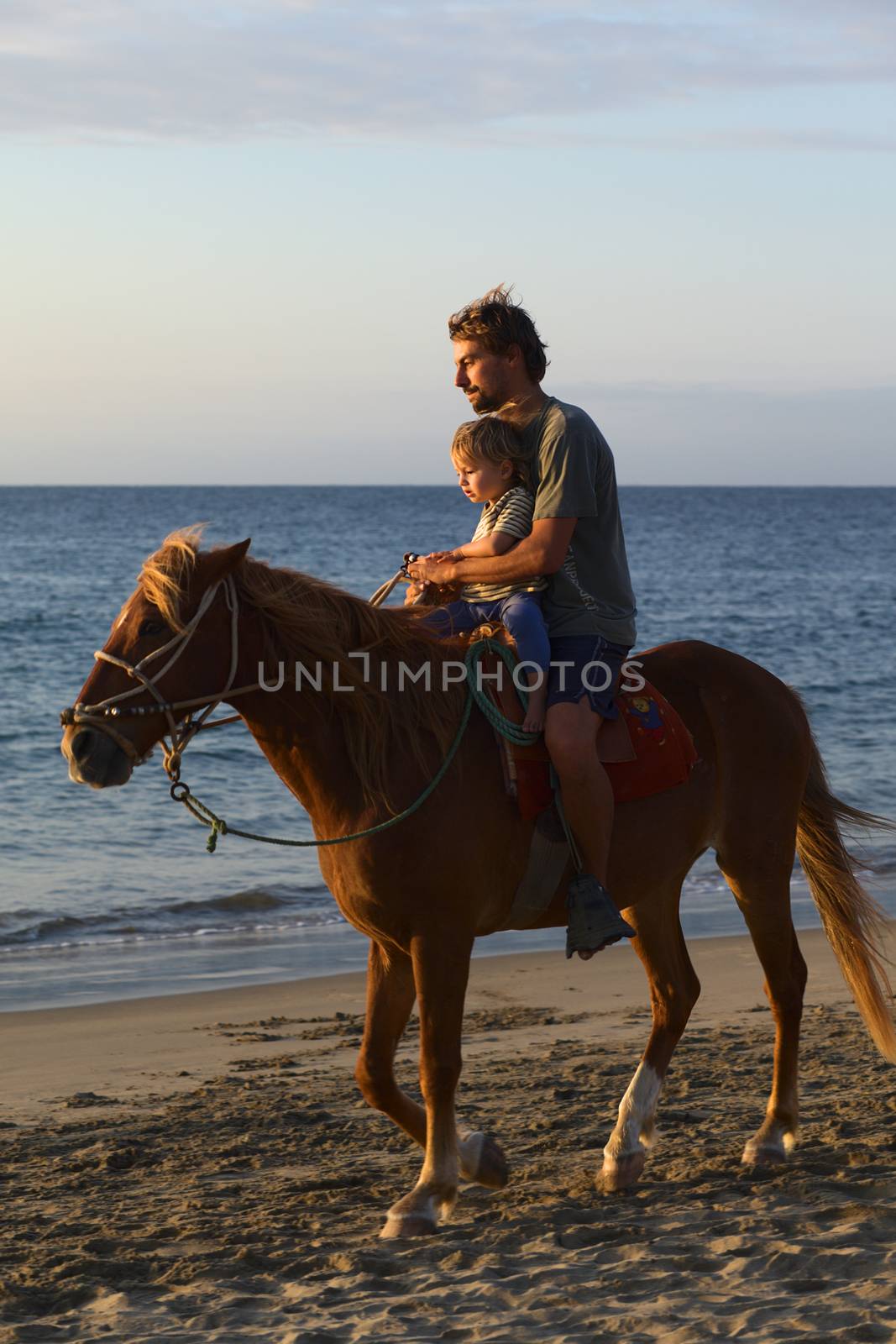 MANCORA, PERU - AUGUST 20, 2013: Unidentified young man and child on horseback on the beach lit by the setting sun on August 20, 2013 in Mancora, Peru. Mancora is a popular beach town in Peru for both Peruvian and foreign tourists.   