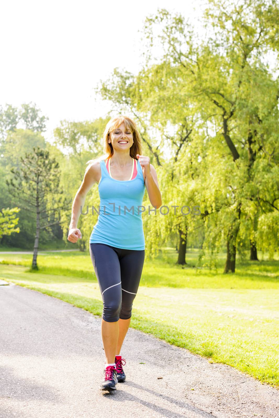 Smiling woman exercising on running path in green summer park