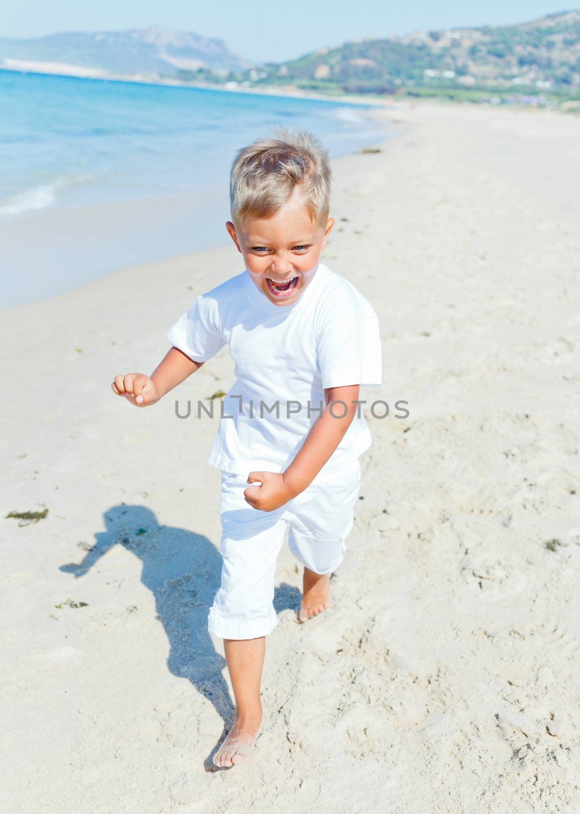 Smiling cute boy runs along the tropical beach.