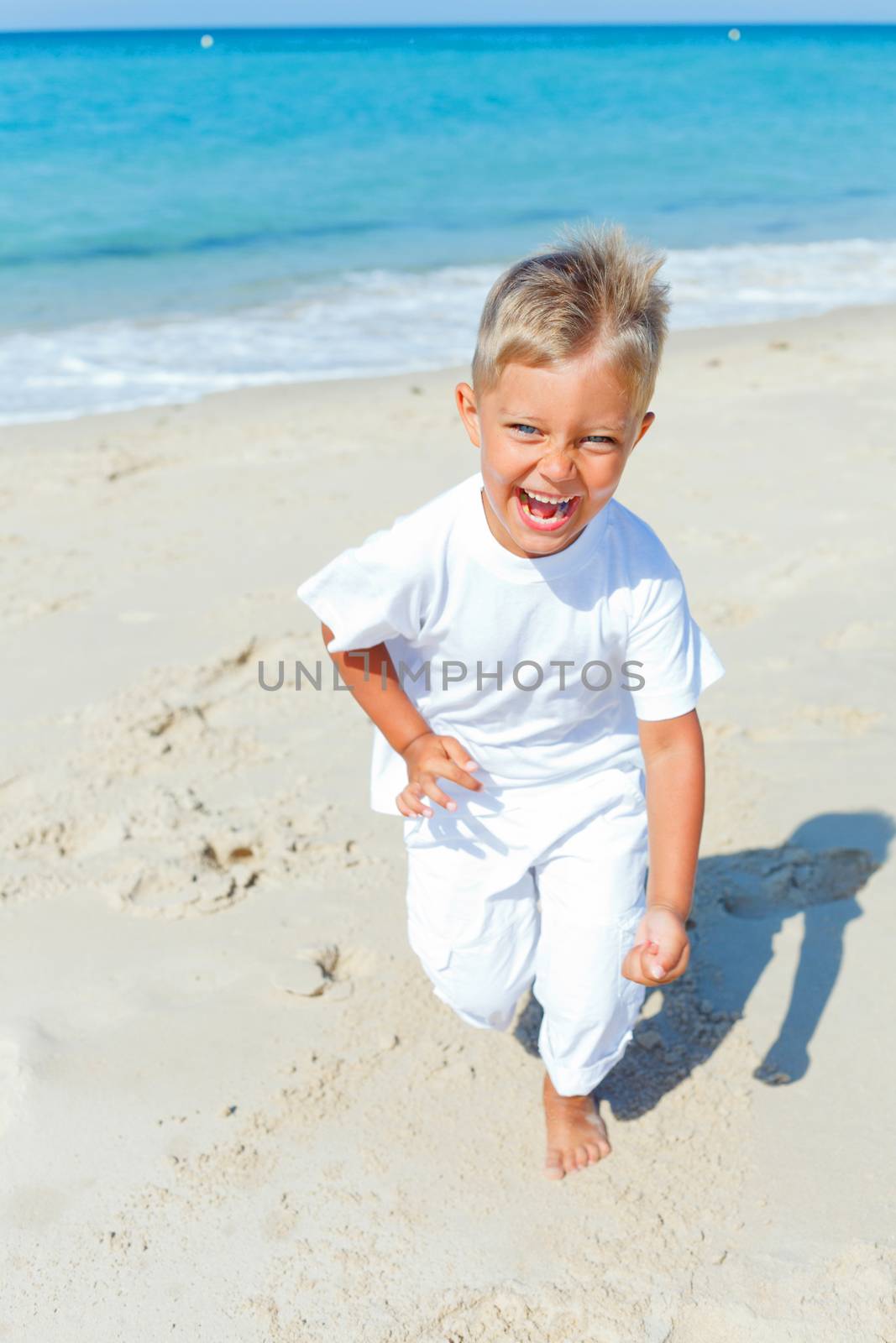Smiling cute boy runs along the tropical beach.