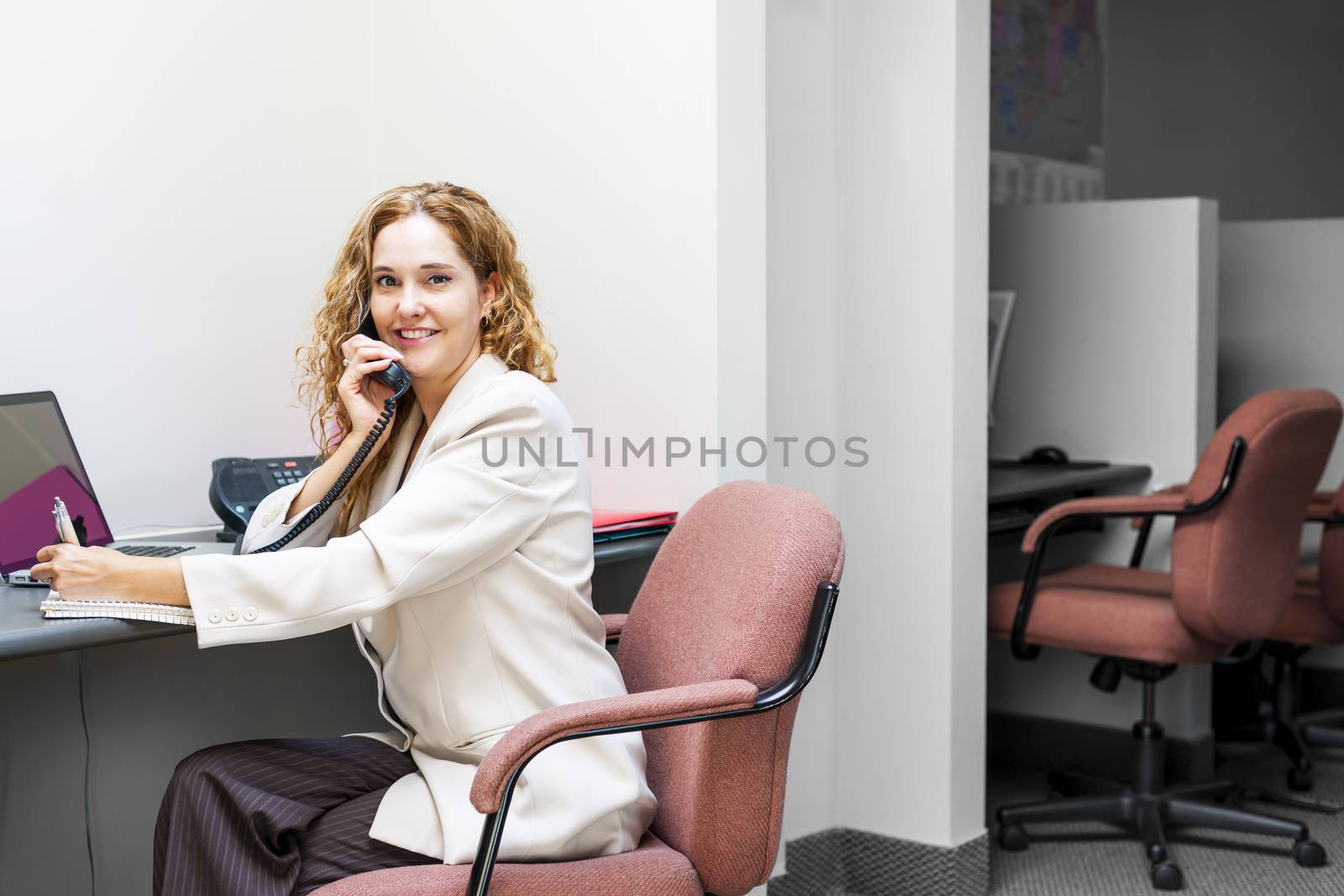 Smiling woman on telephone at office desk by elenathewise