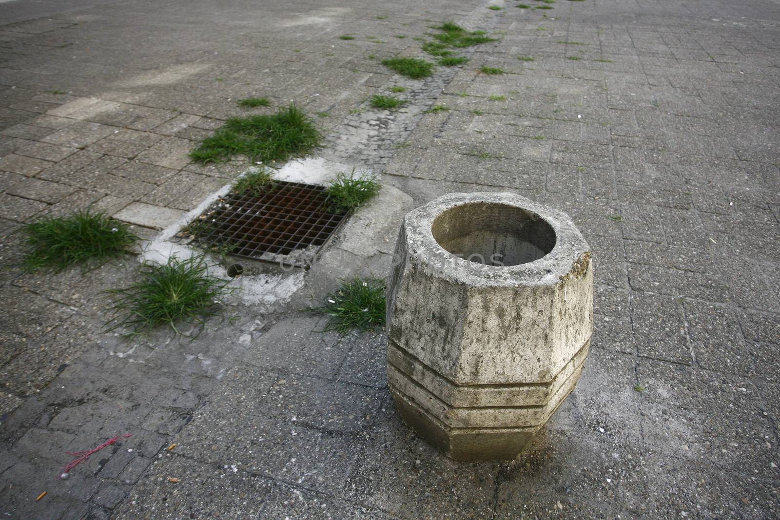 rusty stone trash can in street near manhole