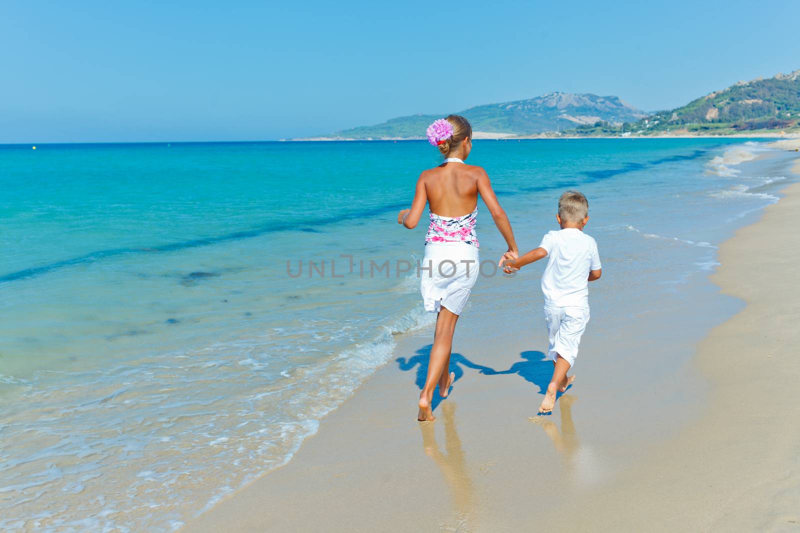 Back view of adorable happy boy and girl runs along beach vacation