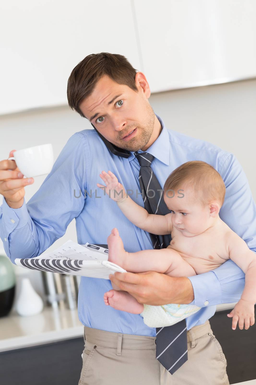 Busy father holding his baby son before work at home in the kitchen