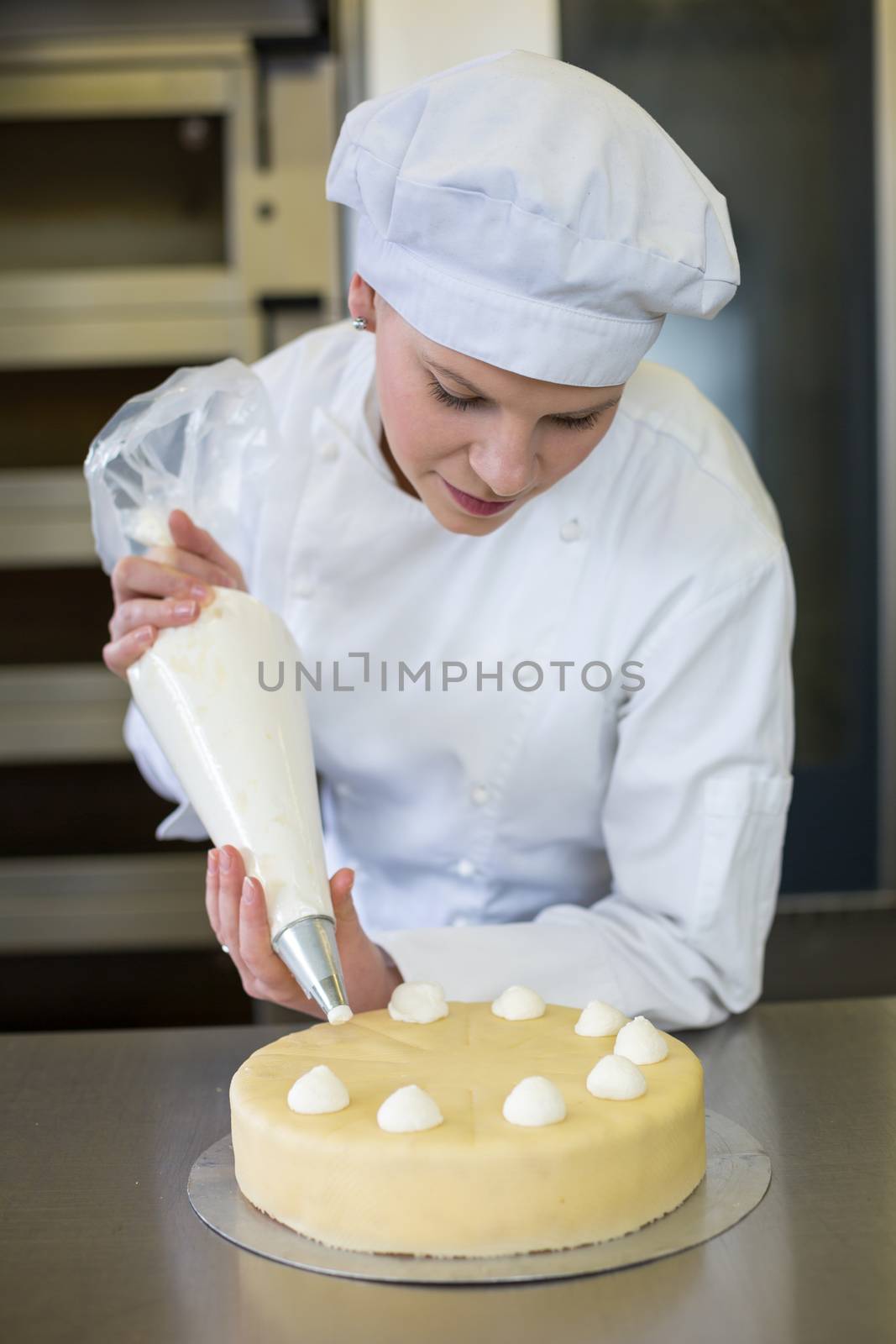 Baker prepares cake in bakehouse with whipped cream by ikonoklast_fotografie