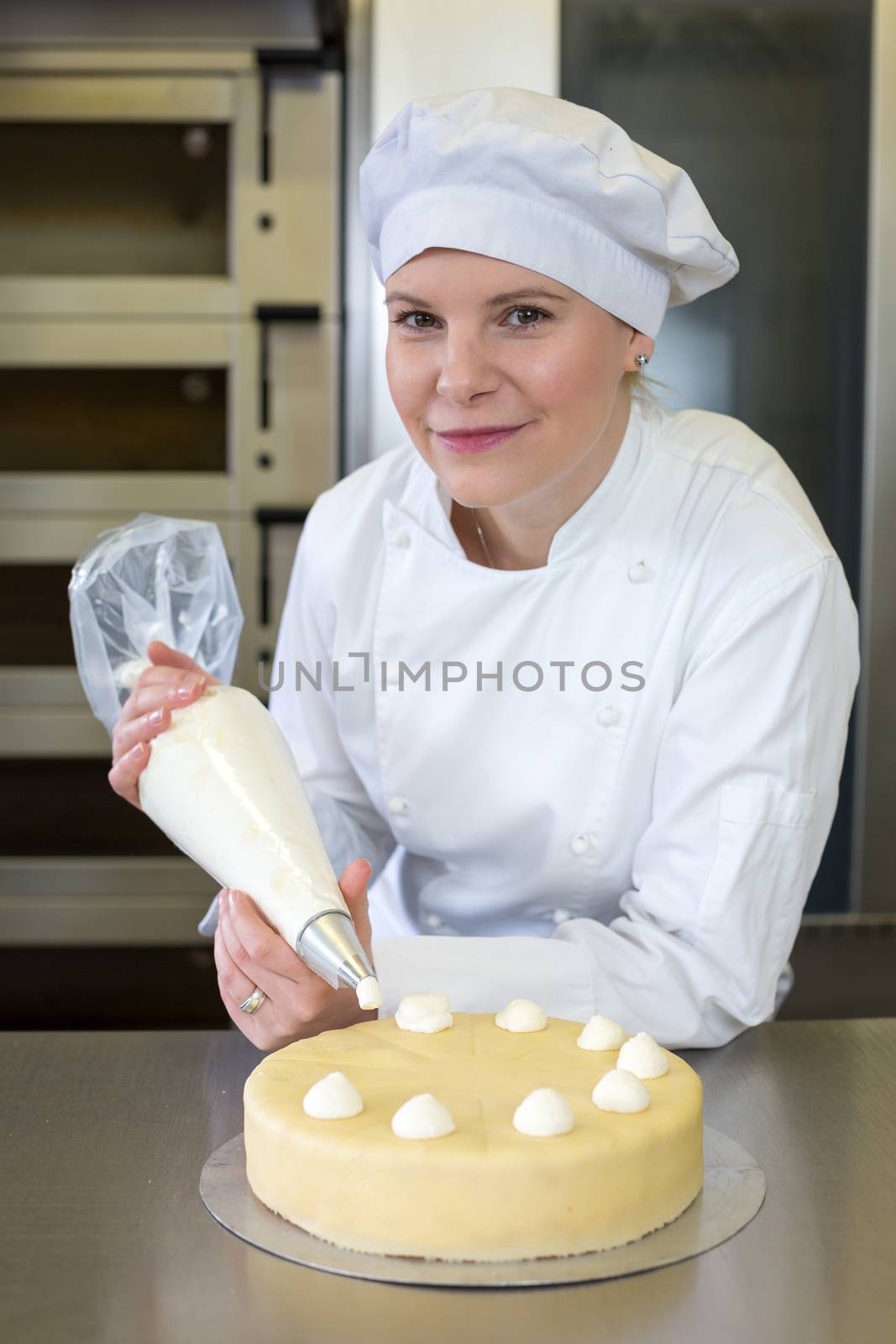Baker prepares cake in bakehouse with whipped cream by ikonoklast_fotografie