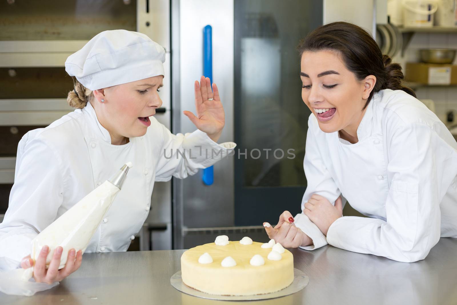 Confectioner apprentice nibbling whipped cream from cake in bakery