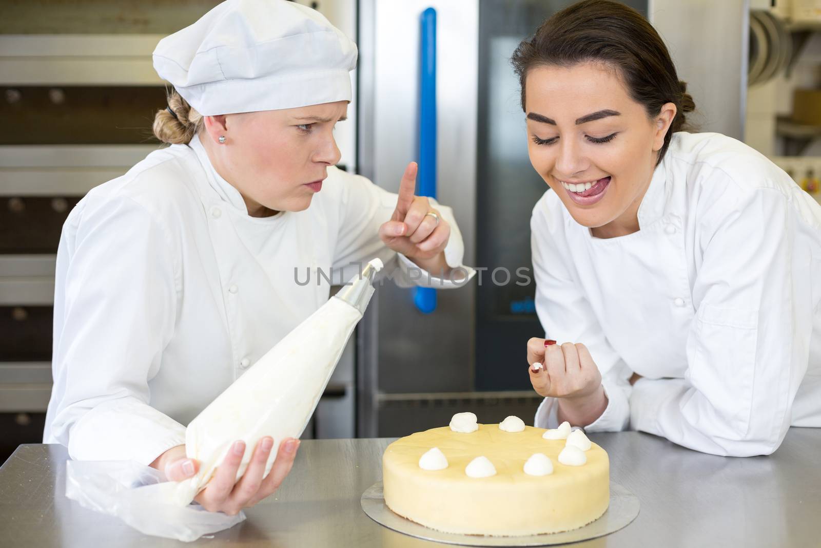 Confectioner apprentice nibbling whipped cream from cake in bakery