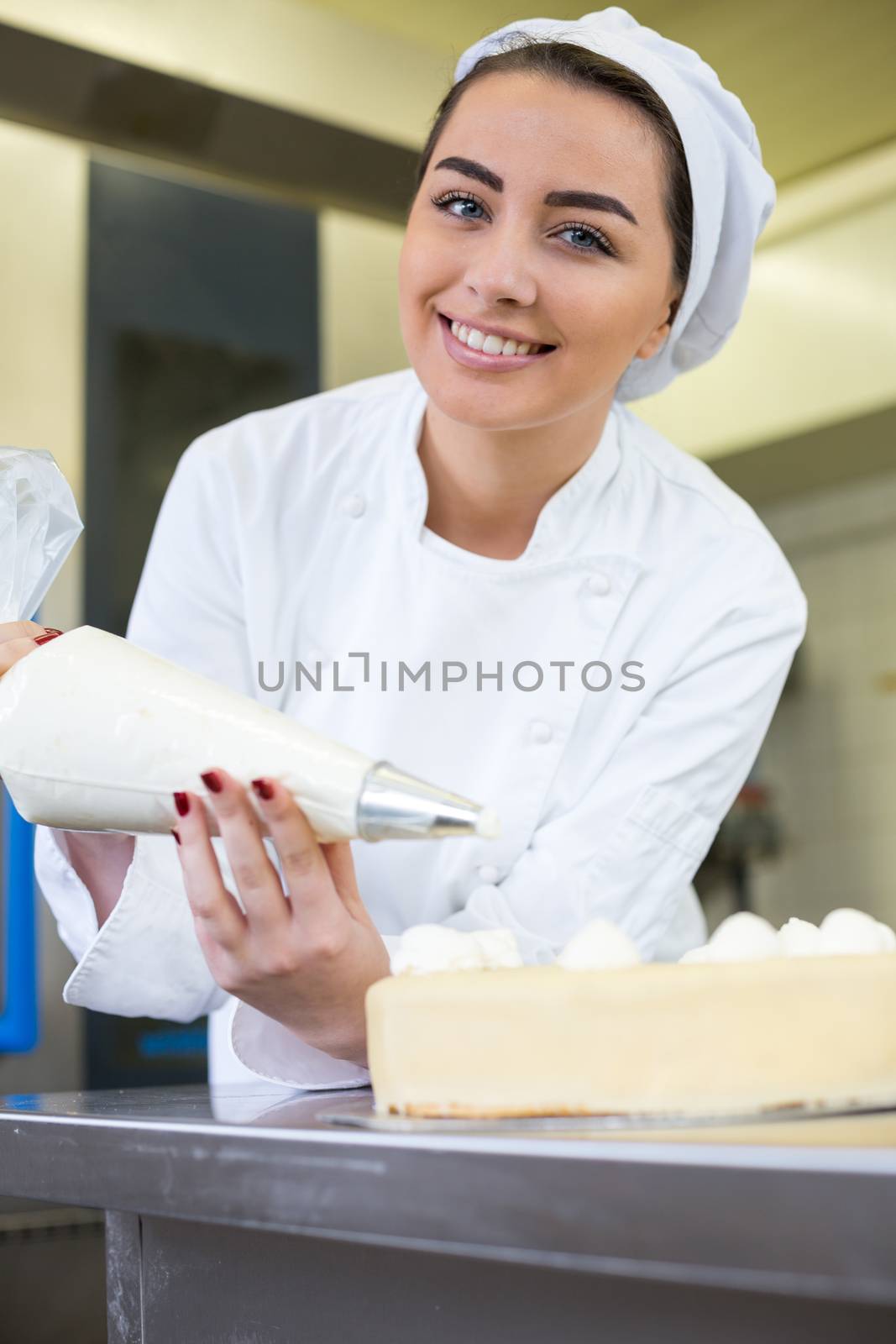 Female baker or confectioner prepares cake with whipped cream