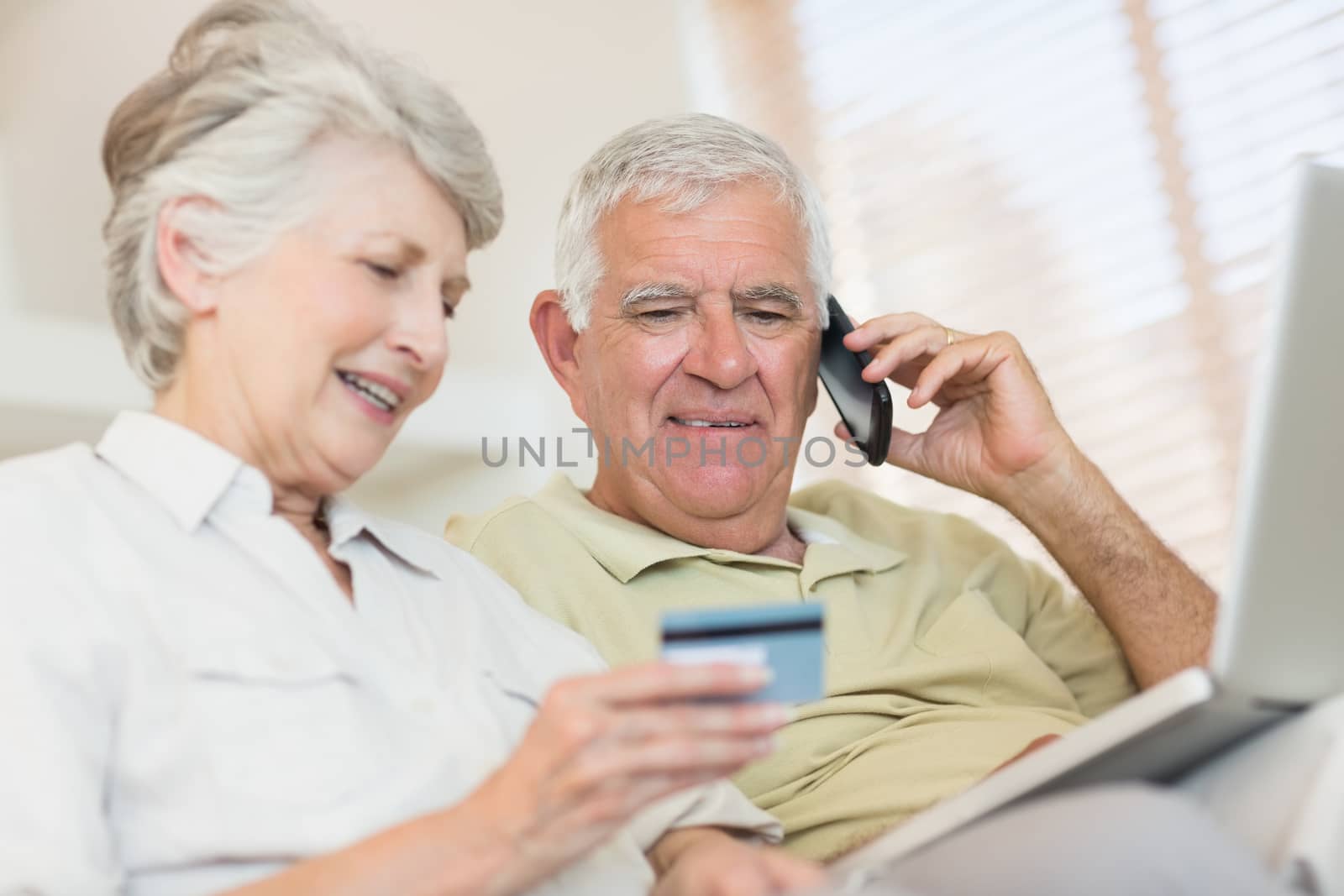 Happy senior couple paying online bill with laptop on the couch at home in the living room