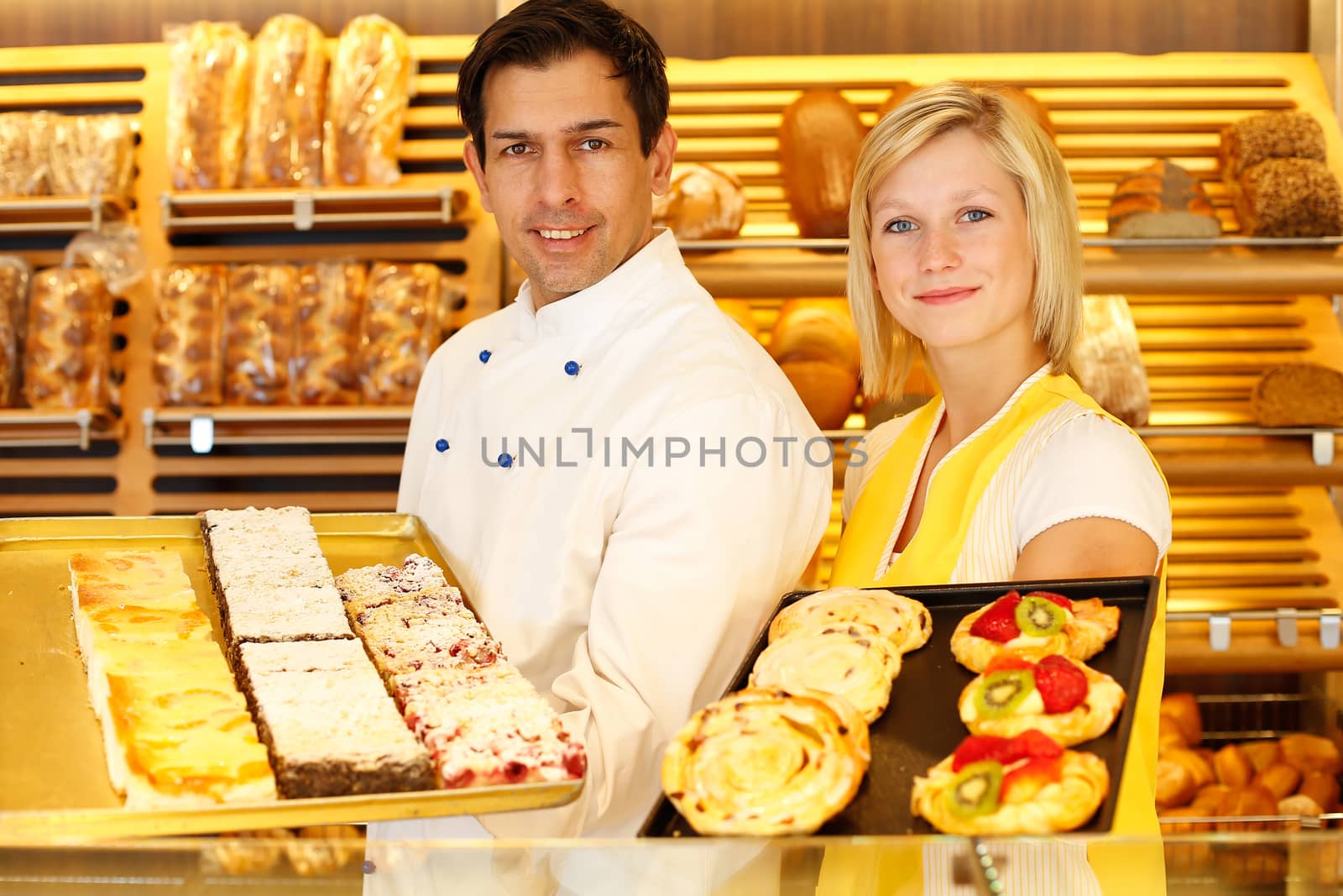 Bakery shopkeeper and baker present different types of pastry in shop