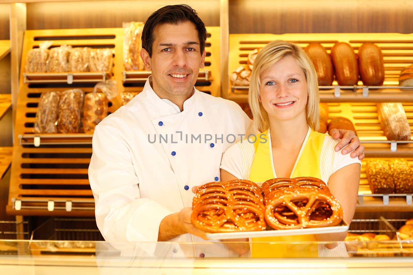 Shopkeeper and baker in Bakery or baker's shop present a tablet full of pretzels