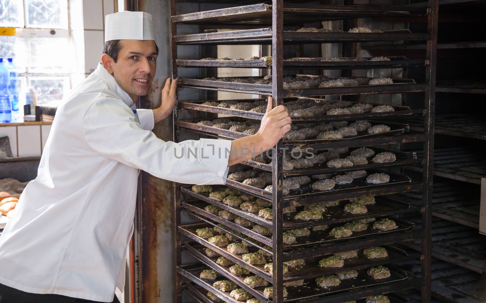 Baker putting a rack of bread into the oven in bakery or bakehouse
