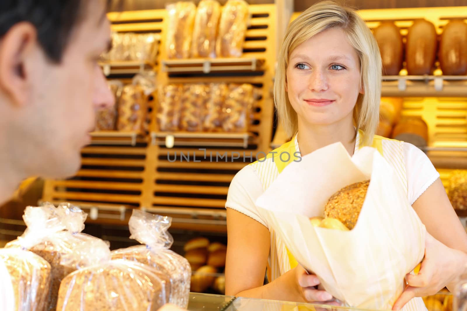 Bakery shopkeeper hands bag of bread over to customer