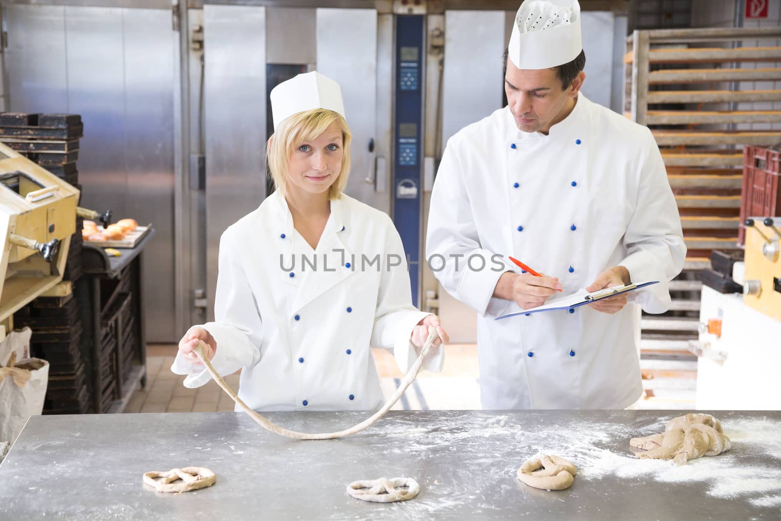 Instructor in bakery teaching apprentice how to form a pretzel out of dough