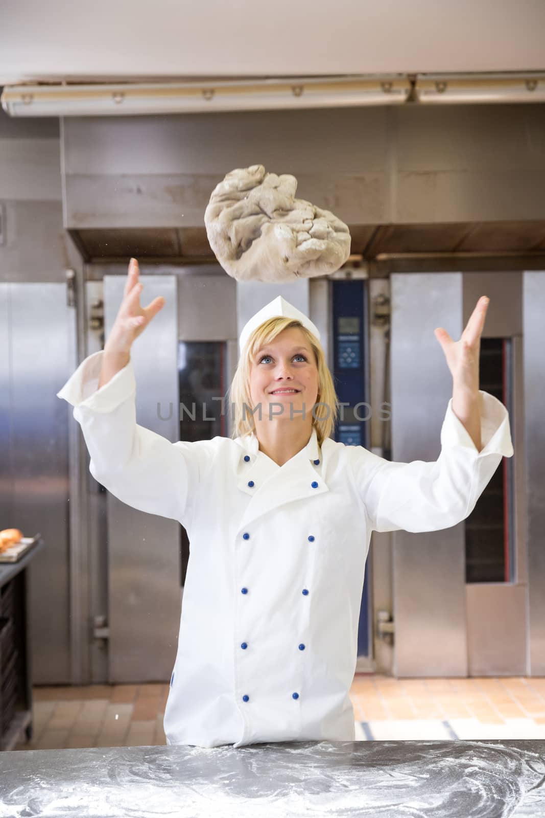 Baker throwing bread dough in bakery or bakehouse by ikonoklast_fotografie