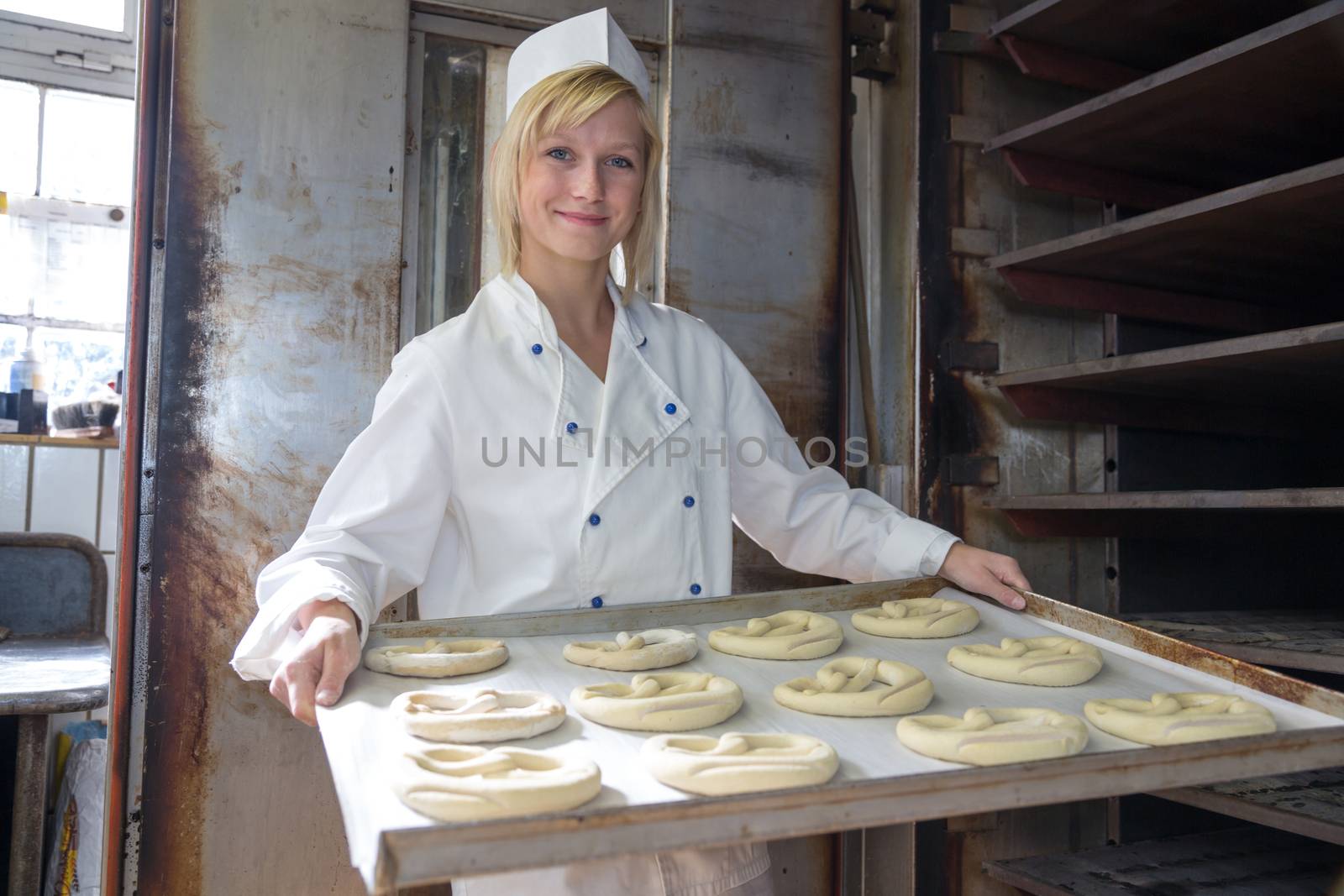 Baker putting pretzels into oven in a bakery by ikonoklast_fotografie