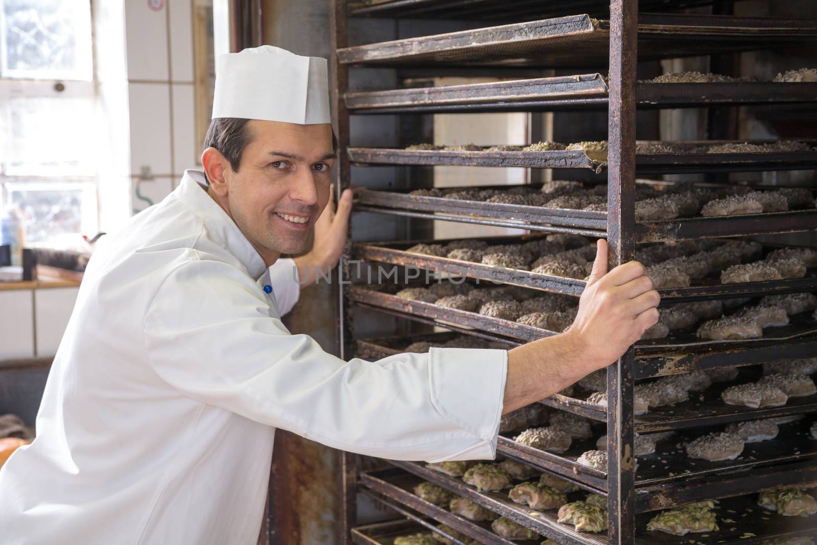 Baker putting a rack of bread into oven by ikonoklast_fotografie